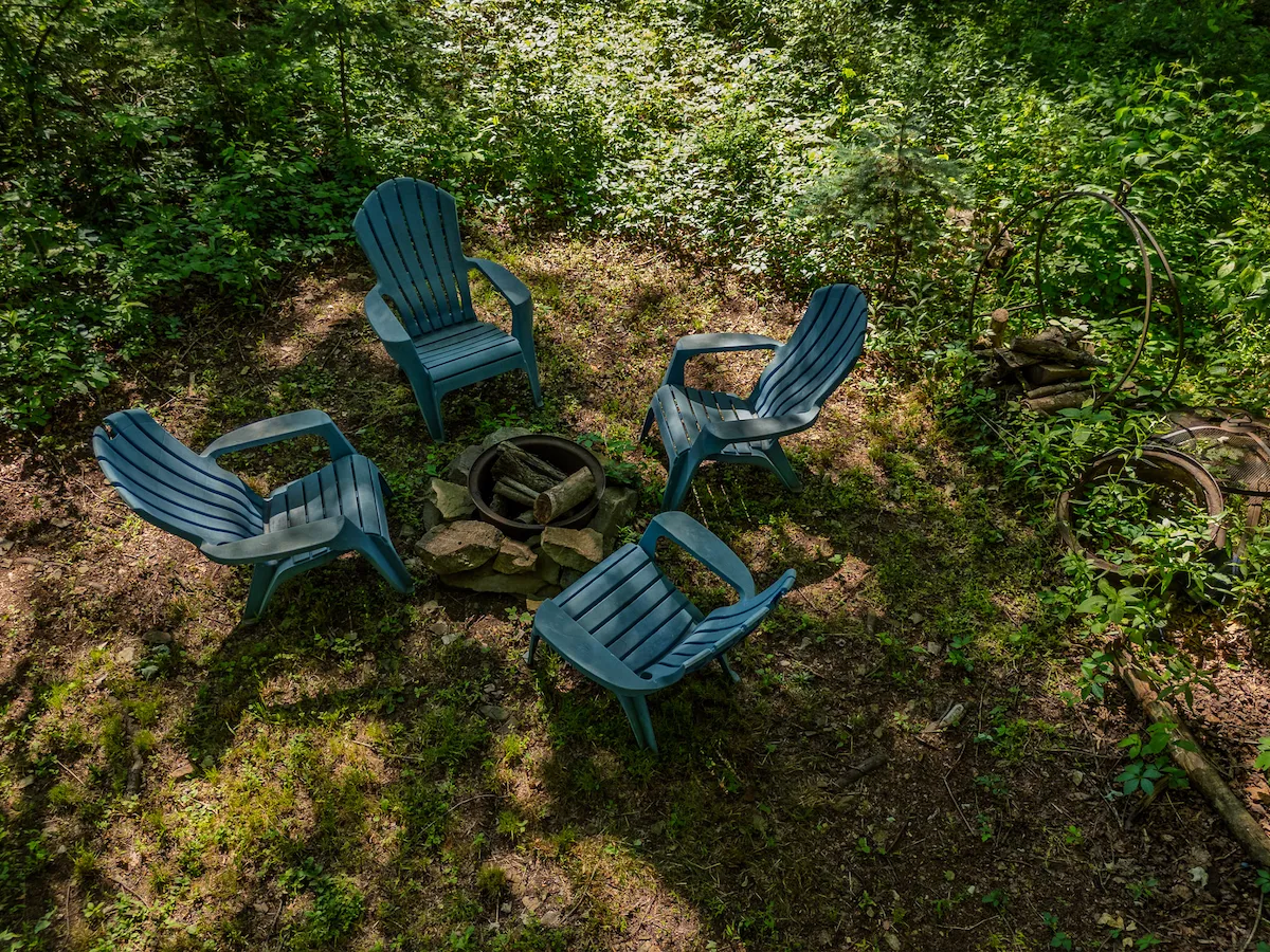 Blue Adirondack chairs gathered around a stone fire pit in the woods