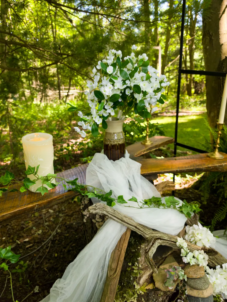 Altar detail — a white bouquet, pillar candle, ivy, and draped tulle on the driftwood altar