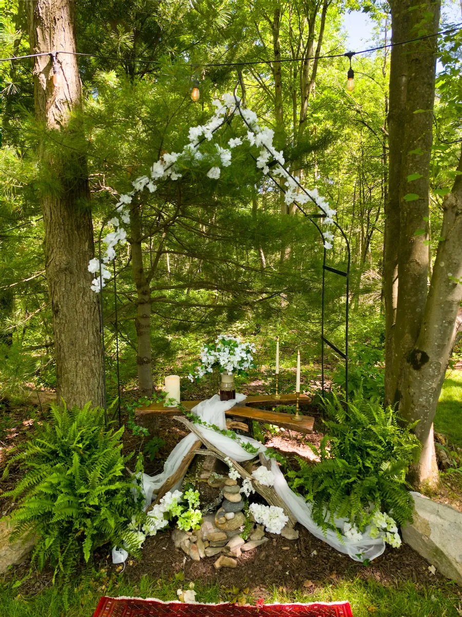 The chapel's flower-wound iron arch altar with candles and ferns in the woods