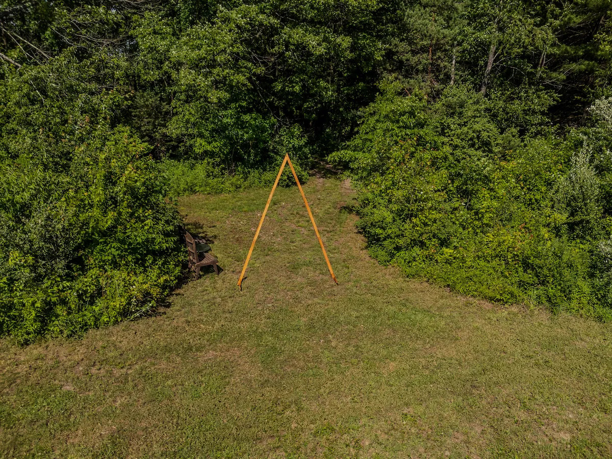 Aerial looking down on the A-frame arch in the clearing, a mown path leading out through the trees into the field