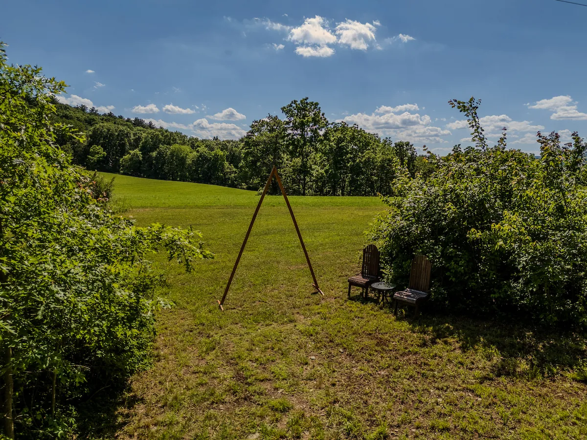 A wooden A-frame ceremony arch in the open field with the Pocono ridgeline beyond