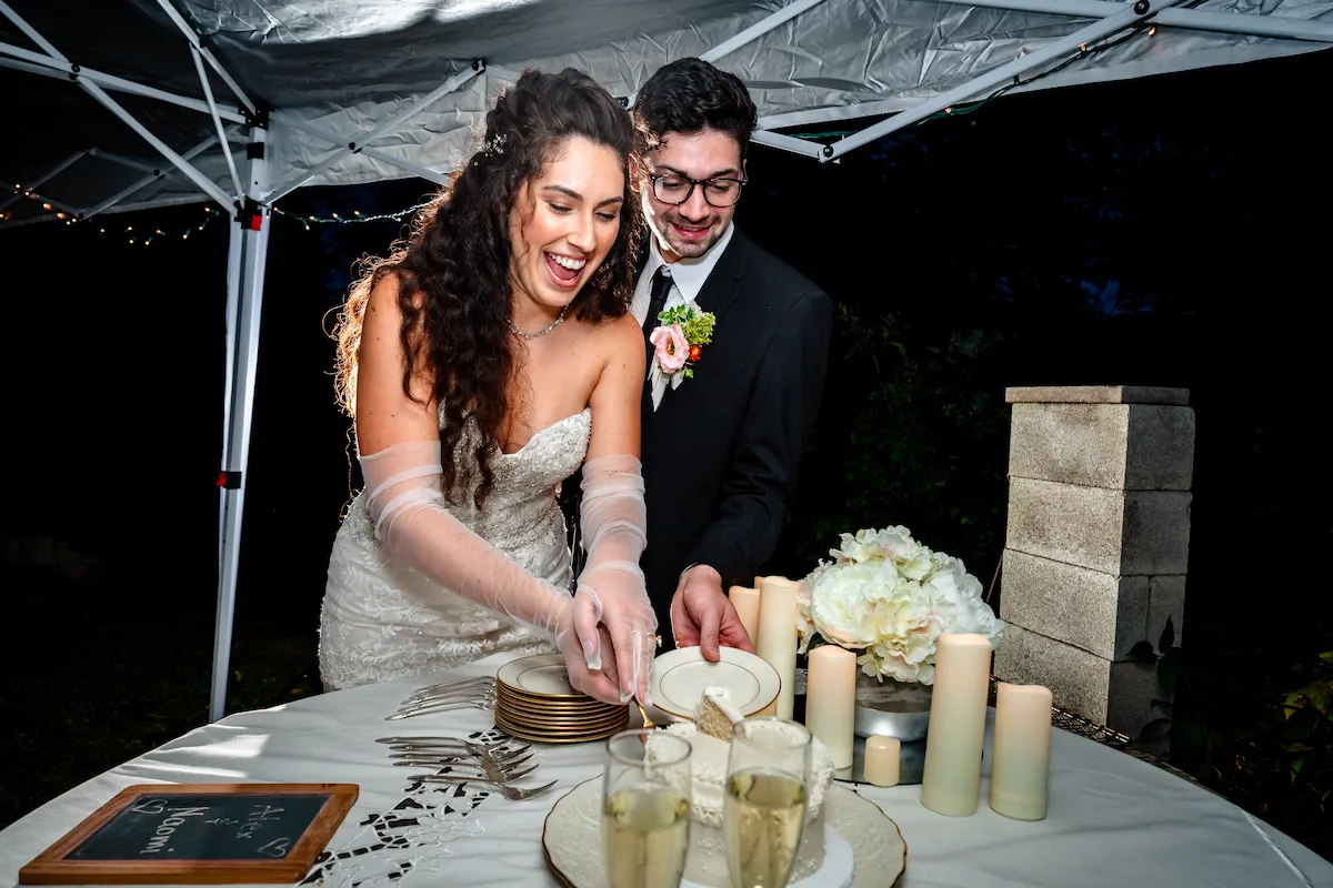 Alex and Naomi cut the cake under the tent, laughing