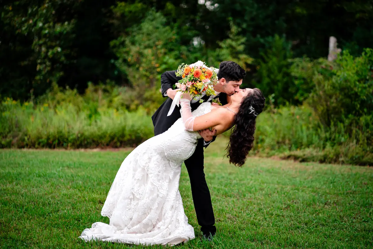 Alex dips Naomi for a kiss in the open field, bouquet in hand
