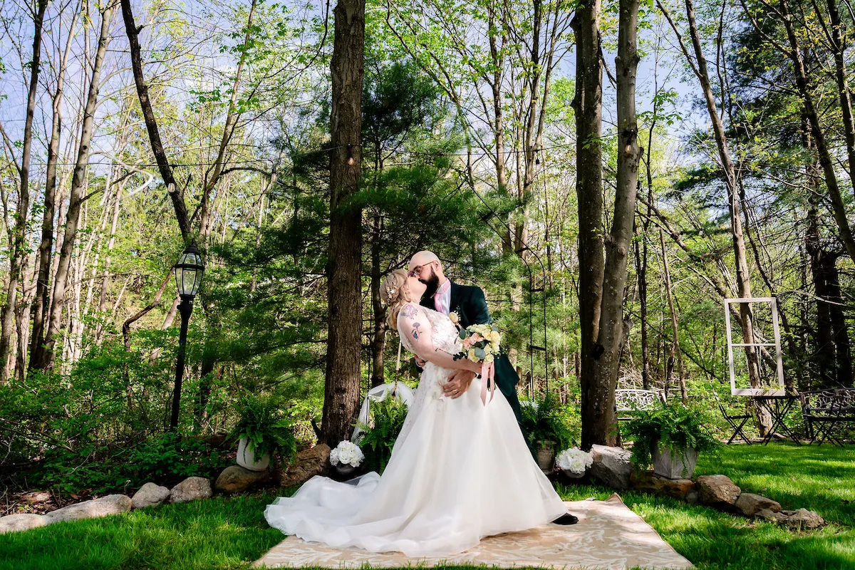 Tera and Matt sit together on a bench in the woods, her gown spread around her