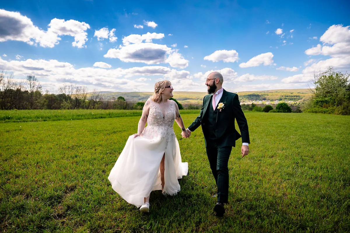 Tera and Matt walk hand in hand across the open field with the ridgeline behind them